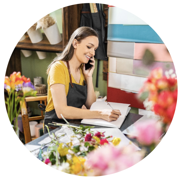 Smiling florist talking on the phone while writing in a notebook at her flower shop.
